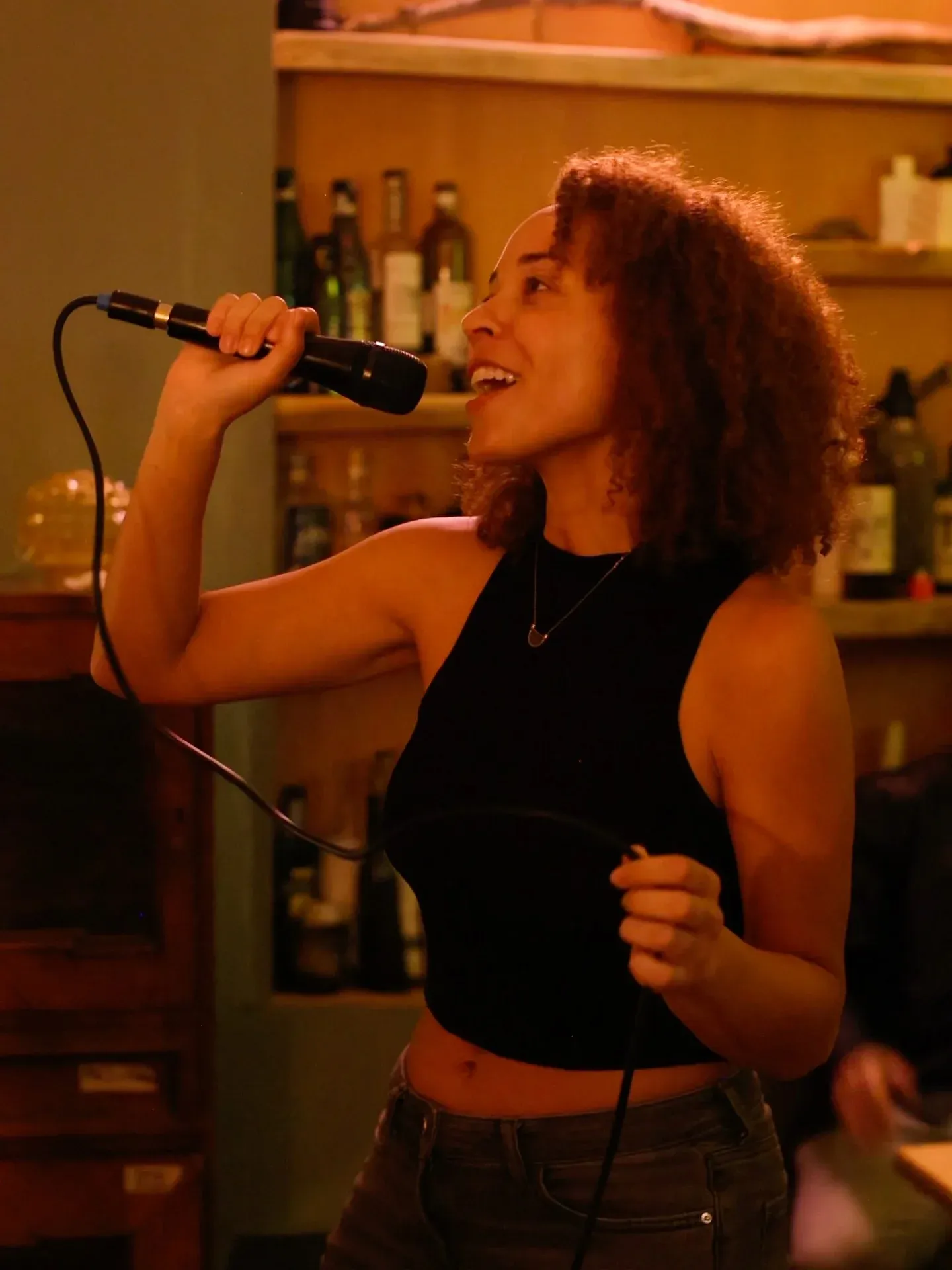 A singer mid-chorus at the microphone in front of the back-bar shelves