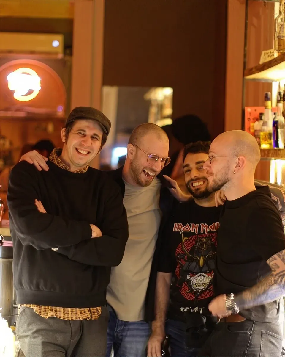 Four friends laughing arm in arm at the bar under the neon sign