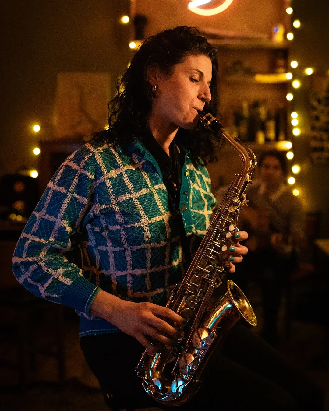 A saxophonist mid-phrase under string lights, the neon sign overhead