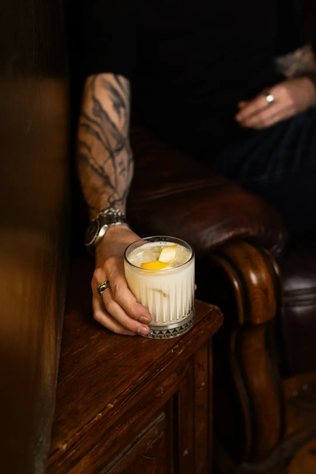 A whisky sour with a lemon twist, in hand in the leather armchair corner
